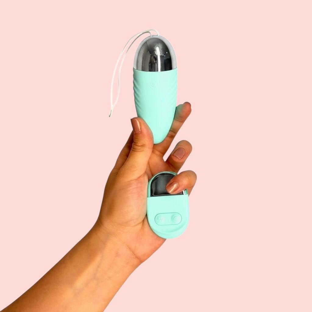 Vibrador Elixir de Amaranto variante azul turqueza con base metálizada, incluye cordón de seguridad y con control remoto, sostenidos en la mano - Edén