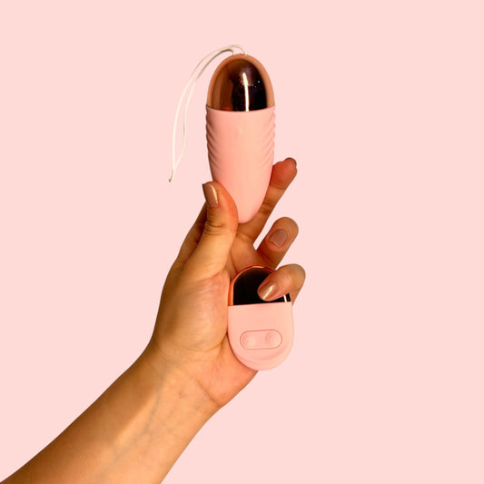 Vibrador Elixir de Amaranto color rosa con base metálizada, incluye cordón de seguridad y con control remoto, sostenidos en la mano - Edén