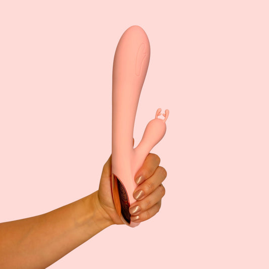 Vibrador Esencia de Lilith color rosa nude con brazo estimulador bifurcado, sostenido en la mano - Edén