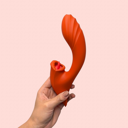 Vibrador Llama de Azahar variante color naranja con masajeador tipo lengua, sostenido en la mano - Edén